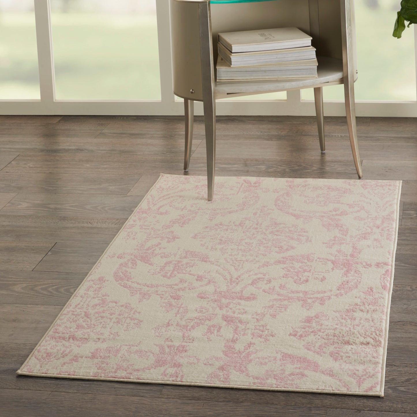 Rectangular pale pink damask rug on dark wood floor beside a modern glass-top side table with books.