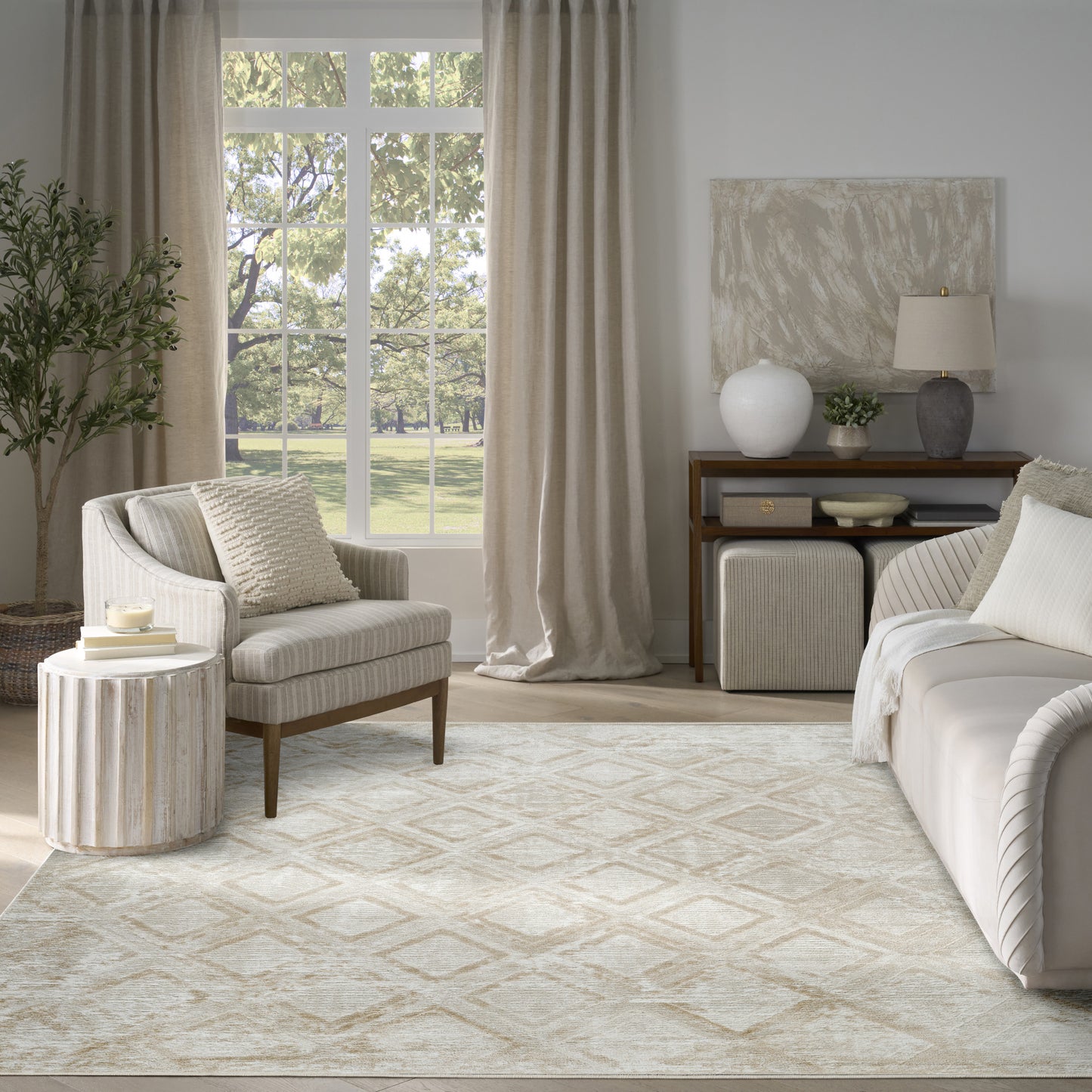 Neutral living room with beige sofa and armchair, geometric rug, tall plant, ribbed side table, and wooden console.