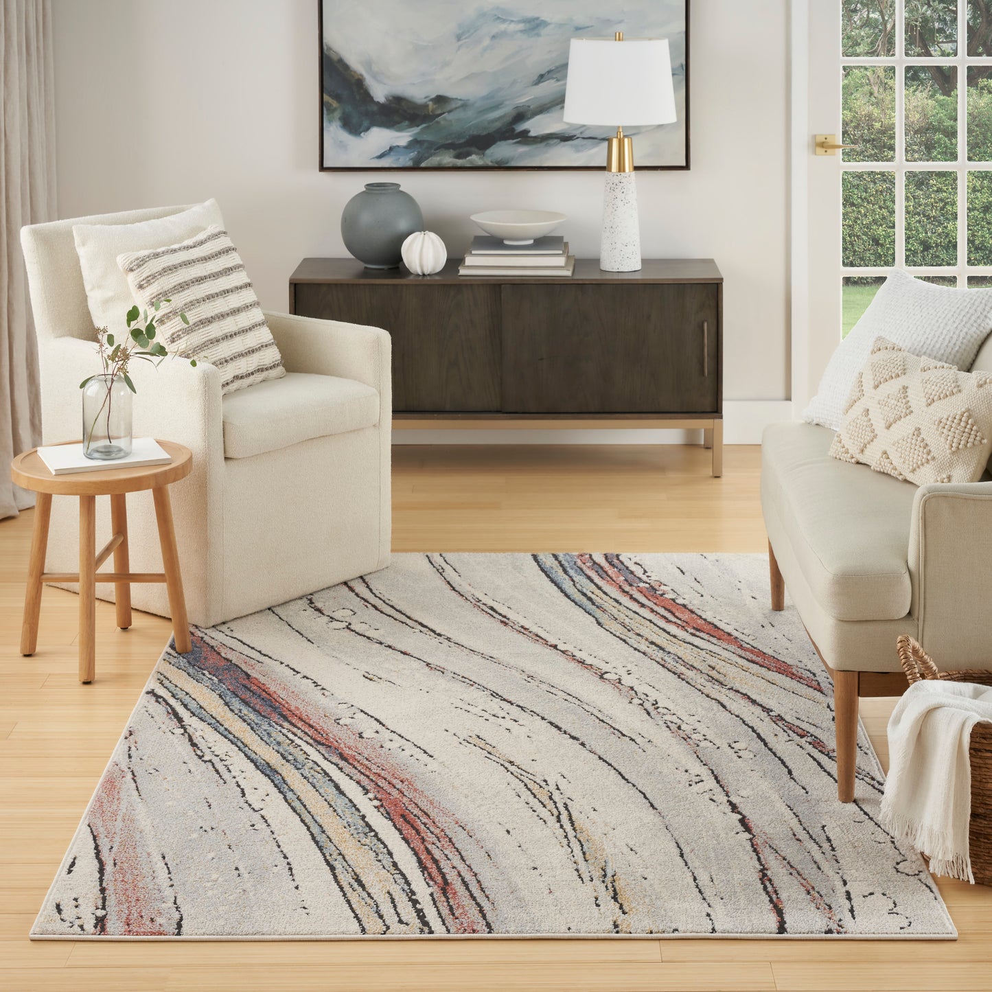 Cozy contemporary living room with cream chairs and a swirled gray-blue-pink rug, light wood floor and dark console
