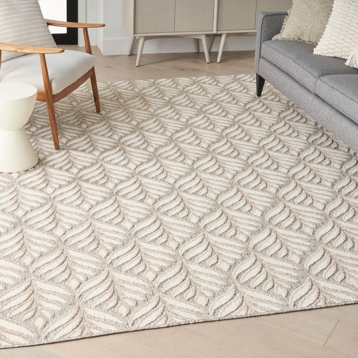 Beige textured area rug with a raised cream and taupe leaf pattern in a modern living room with a gray sofa and wooden chair