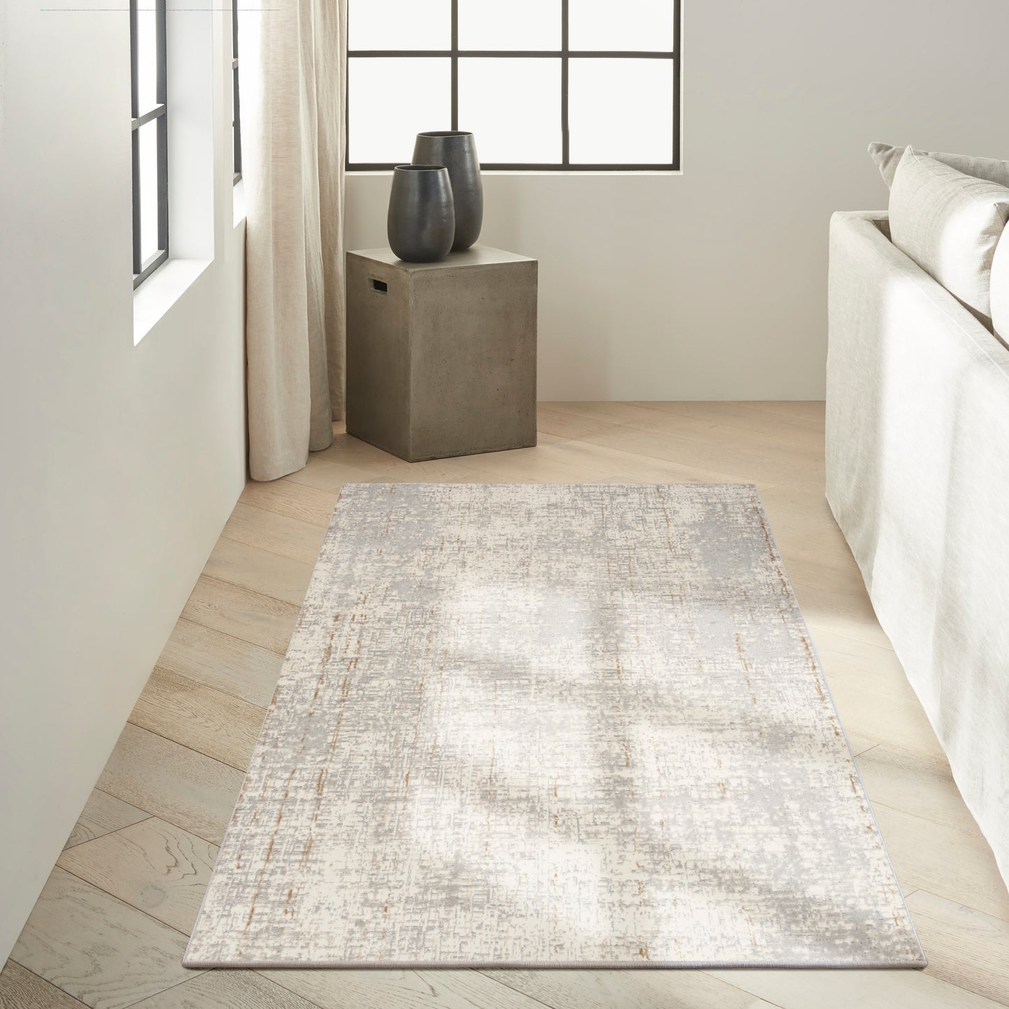 Neutral-toned abstract rug on light wood floor beside a concrete block side table with two dark ceramic vases.