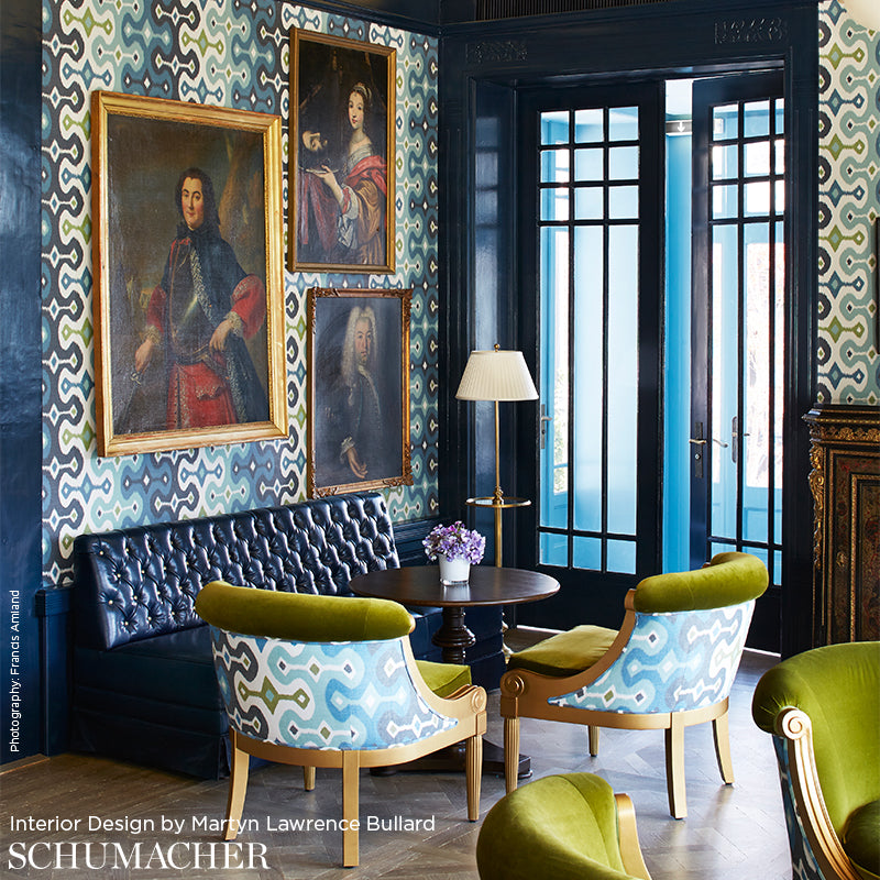 Lux living room with teal geometric wallpaper, gold-framed portraits, navy tufted sofa, blue-and-lime chairs.