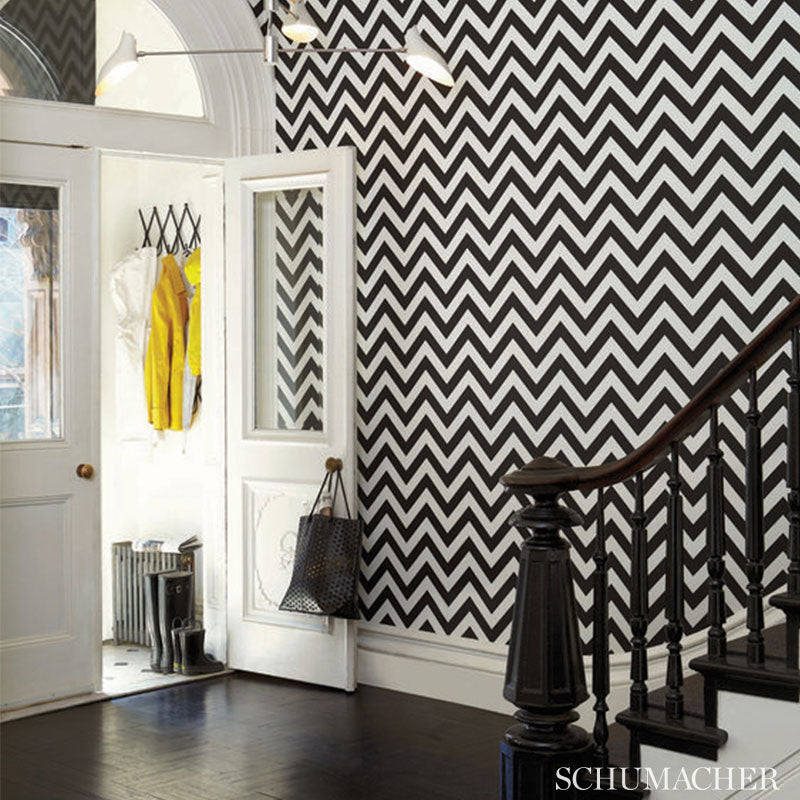 Entryway with bold black-and-white chevron wallpaper, white doors and mirror panels, a yellow coat and dark wood staircase.