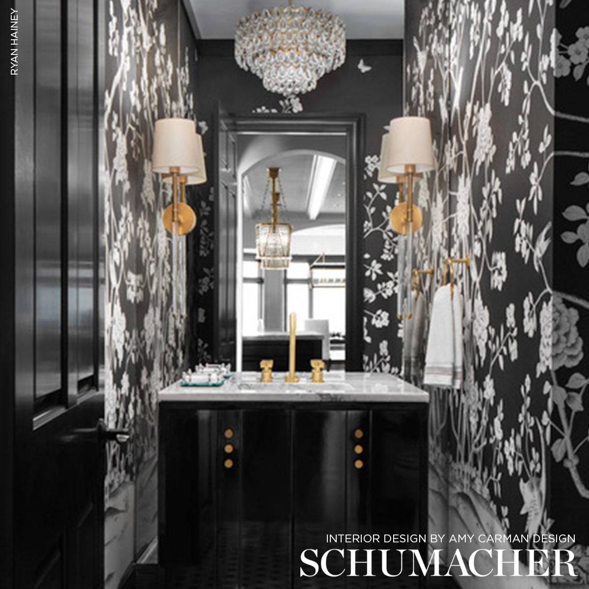 Luxurious black vanity with marble top, gold hardware amid black-and-white floral wallpaper, crystal chandelier and sconces