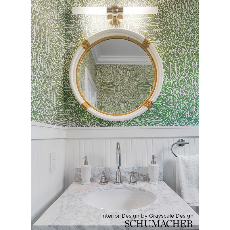 Round gold-framed mirror above a marble bathroom vanity with palm-leaf wallpaper and white wainscoting.
