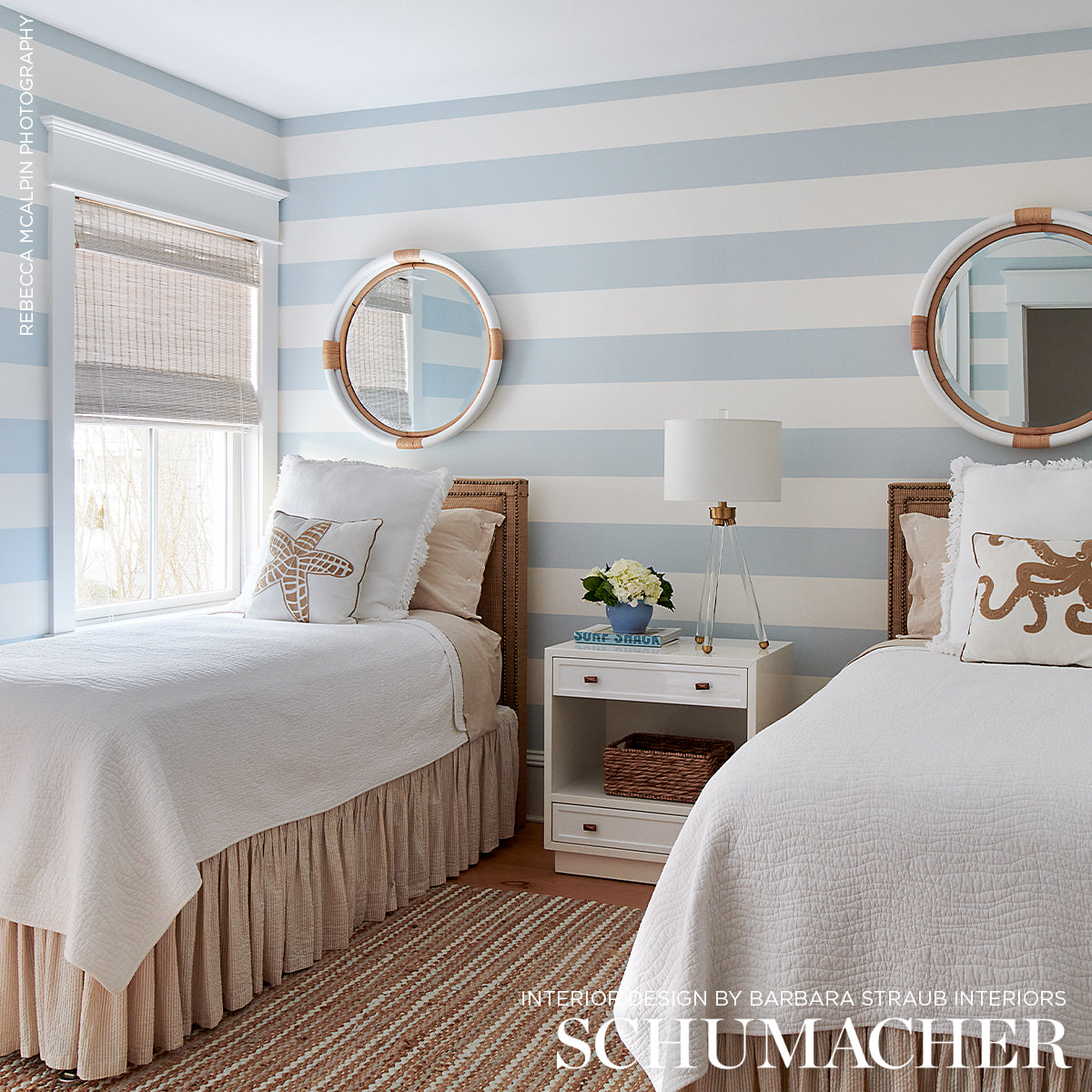 Coastal twin bedroom with light blue-and-white striped walls, two beds, round copper mirrors, white nightstand, lamp.