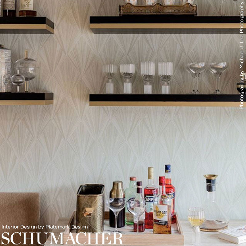 Living room bar with glassware on black floating shelves and liquor bottles on light wood counter against geometric wallpaper.