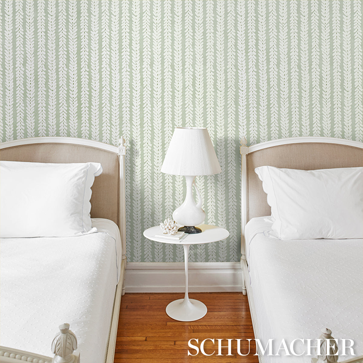 Twin bedroom with mint-green wallpaper, white bedding, beige headboards and round white pedestal table with lamp.