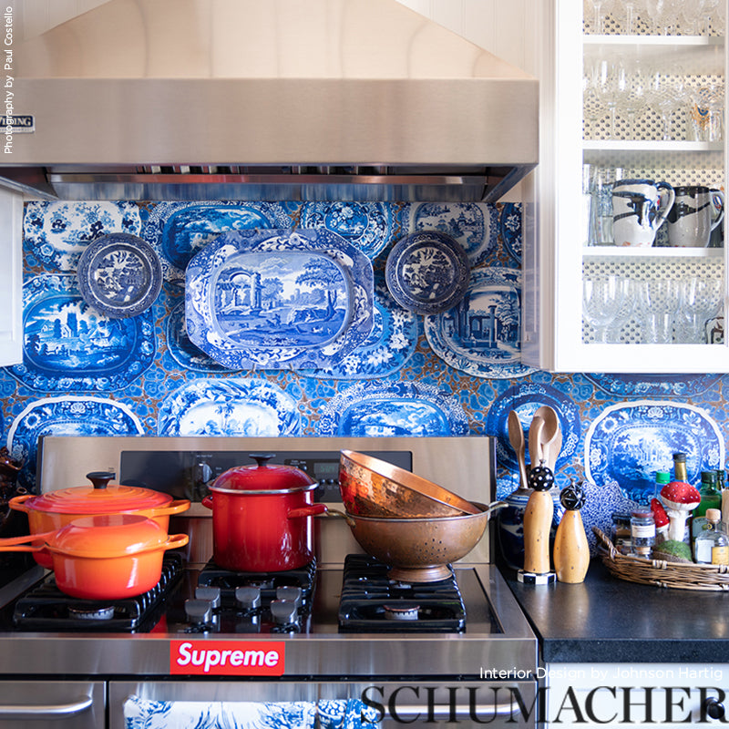 Blue and white Delft-style porcelain plates and bowls as backsplash over a stainless gas range with orange pots and a copper mixing bowl.