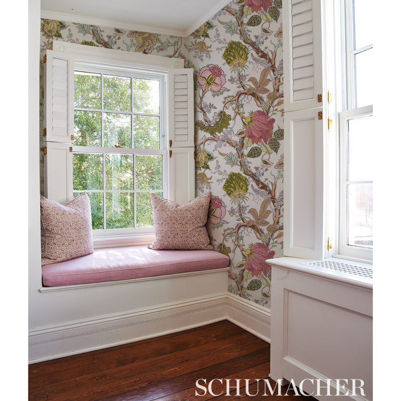 White window-seat nook with pink cushions, Schumacher floral wallpaper, white shutters, and dark hardwood floor.