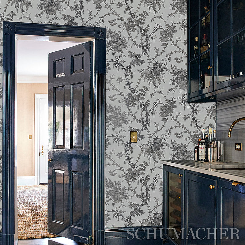 Dark navy paneled door opens to beige foyer; grey botanical wallpaper, navy cabinets, marble countertop and wine cooler.
