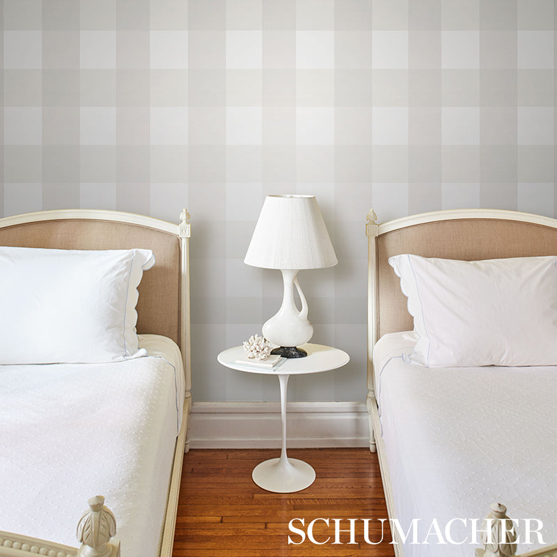 Twin bedroom with white bedding, round white nightstand between beds, lamp, gray checkered wallpaper, wooden floor.