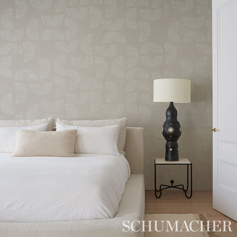 Ivory on neutral wallpaper in a bedroom, with white bedding, beige pillows, and a black ornate lamp on a small metal side table.