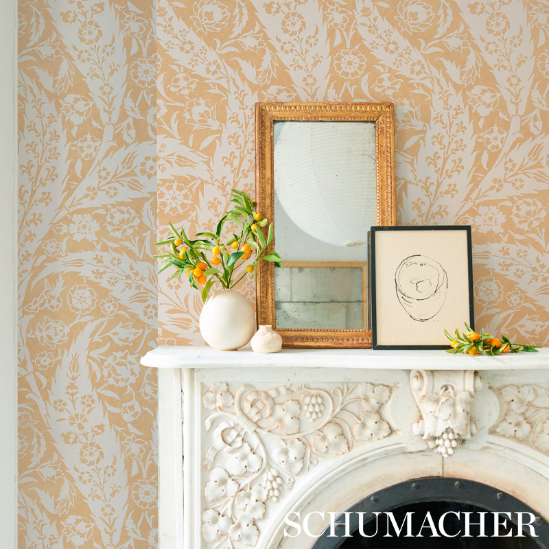 White ornate mantel with floral carvings, gold mirror frame, vase of orange blossoms and a sketch frame on beige wallpaper.
