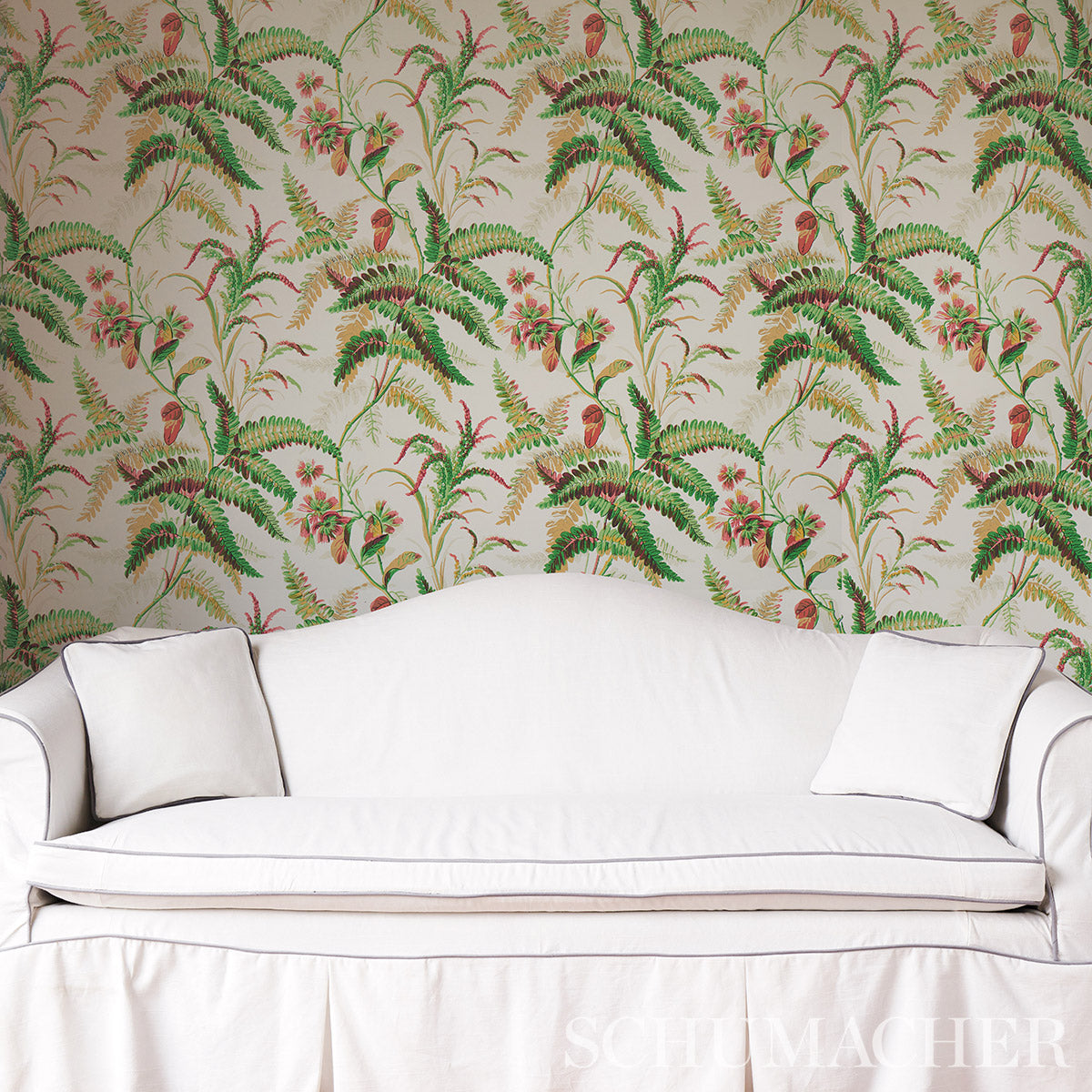 Cream sofa with two white cushions against tropical fern wallpaper with pink flowers.