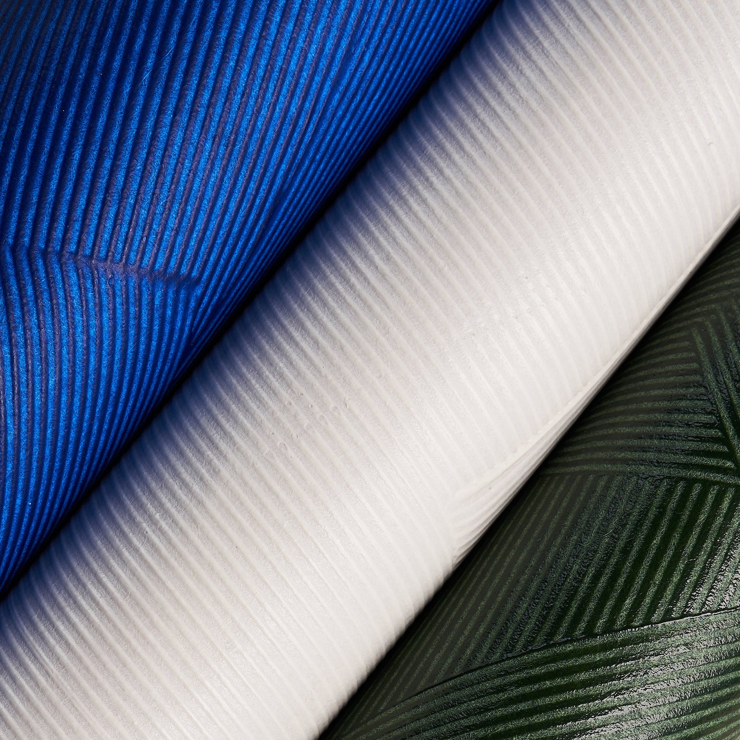 Ribbed wallcovering rolls in royal blue, white and forest green; close-up texture with diagonal folds.