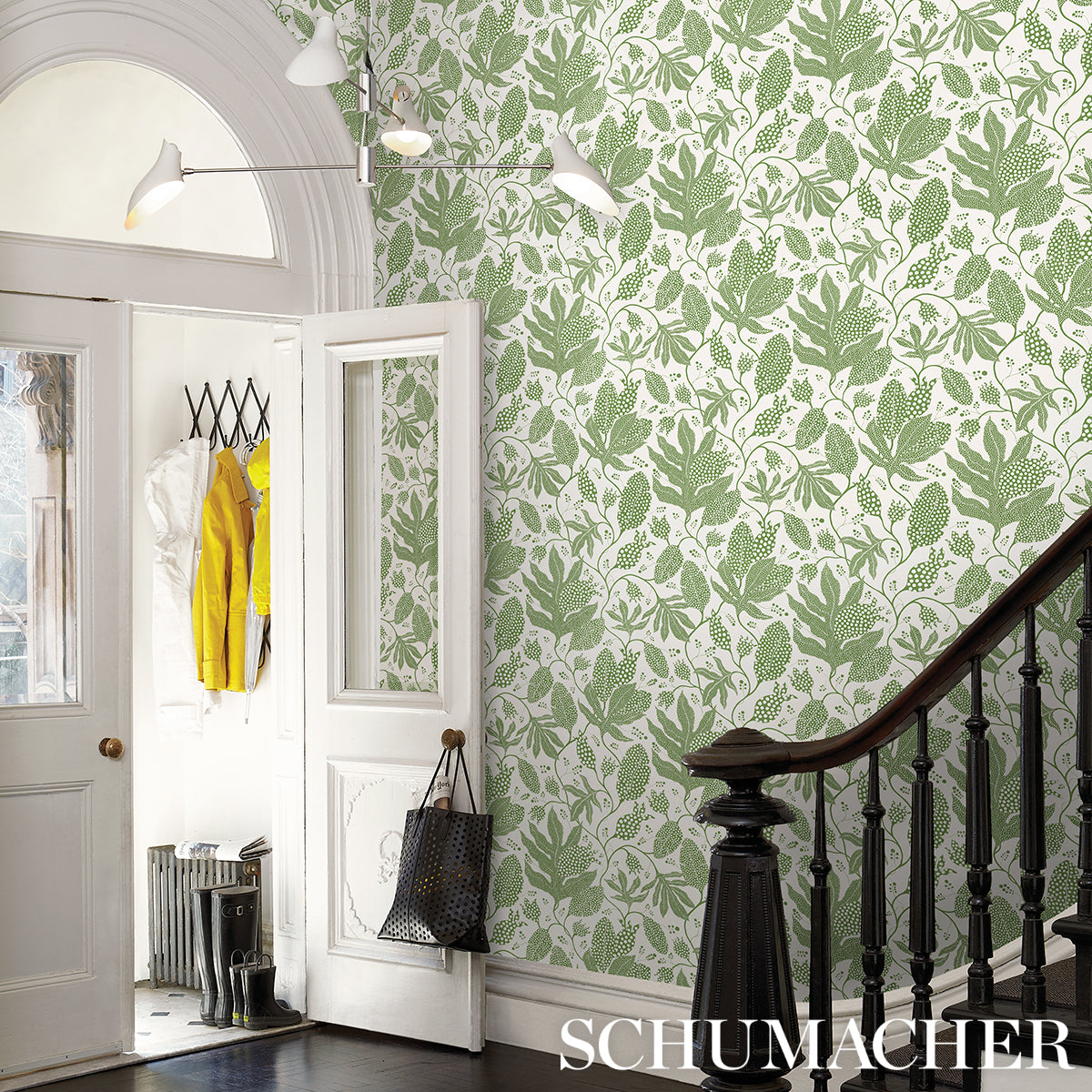 Entryway with green and ivory polka dot jungle wallpaper, white panel doors, black staircase railing, and a yellow coat with a tote bag.