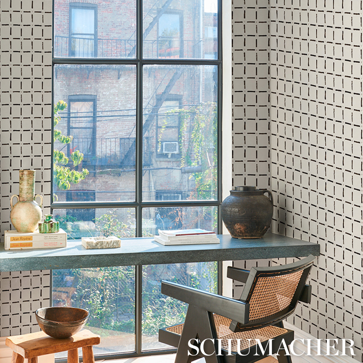 Industrial-style home office with blue-gray desk, cane-back chair, large grid window, tiled walls, and vases with books.