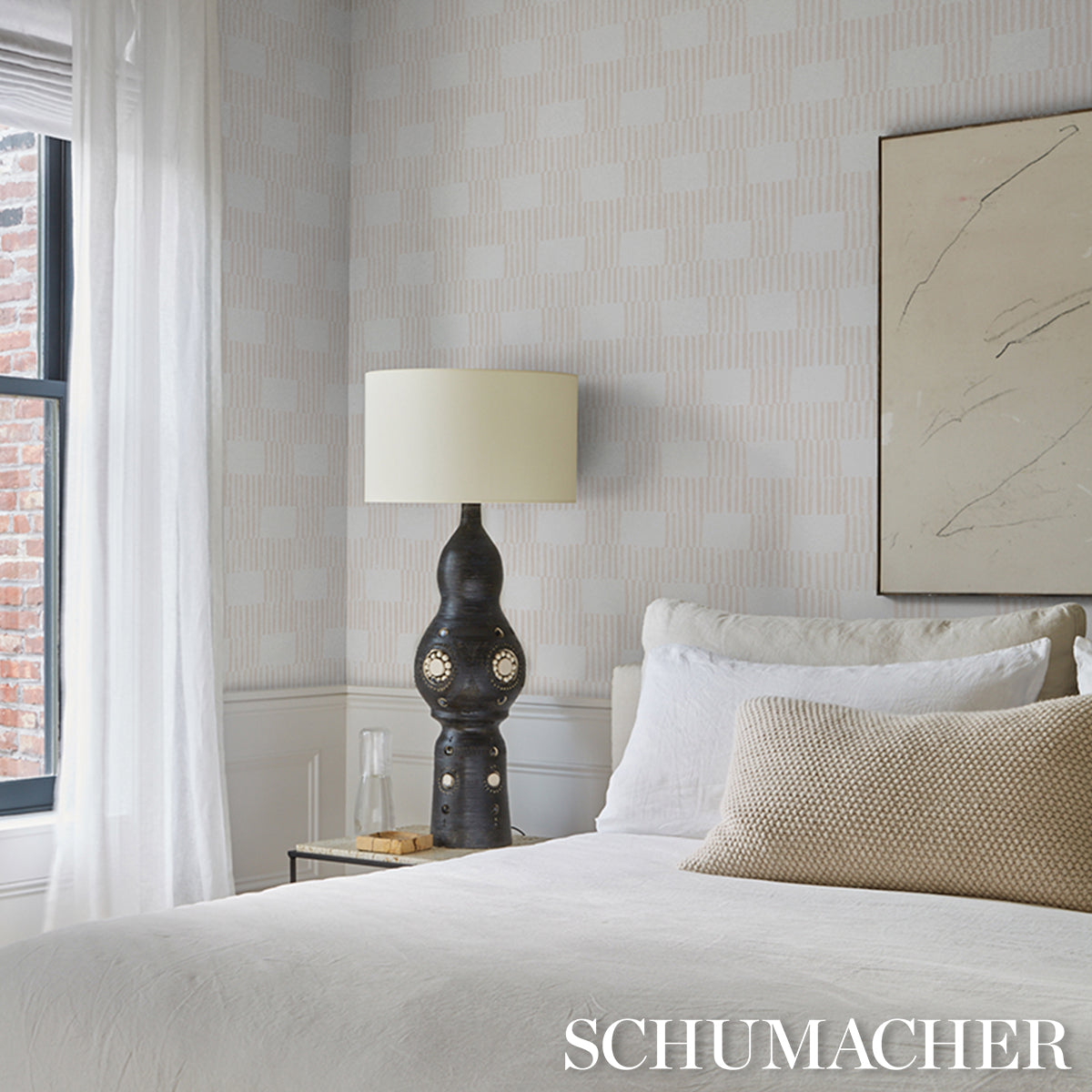 Dark sculptural ceramic bedside lamp with cream shade on glass-topped nightstand, beige bedding, modern bedroom.