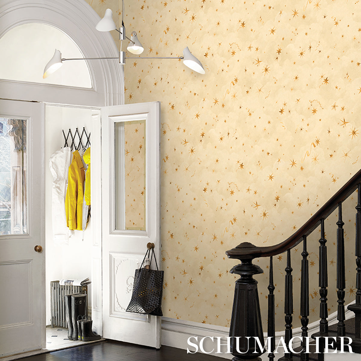 Multi-arm ceiling light in an entryway; beige star wallpaper on the walls, white doors, black staircase railing, closet with a yellow coat.