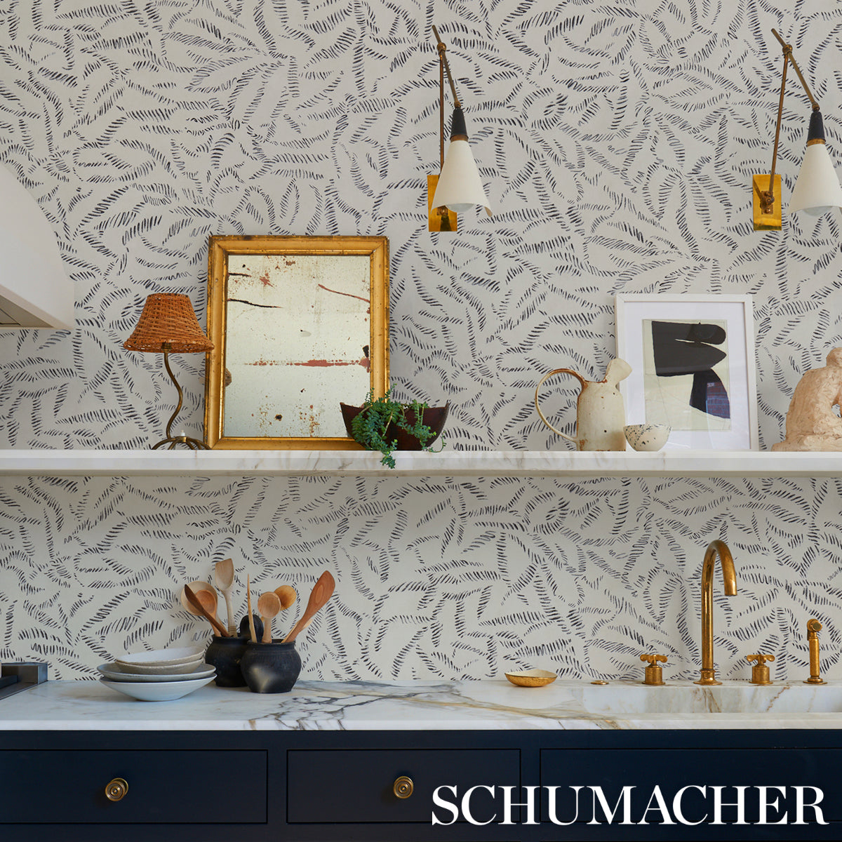 Kitchen with charcoal leaf bloom wallpaper, white marble counter, navy cabinets, gold faucet, pendant lights, and art frames.