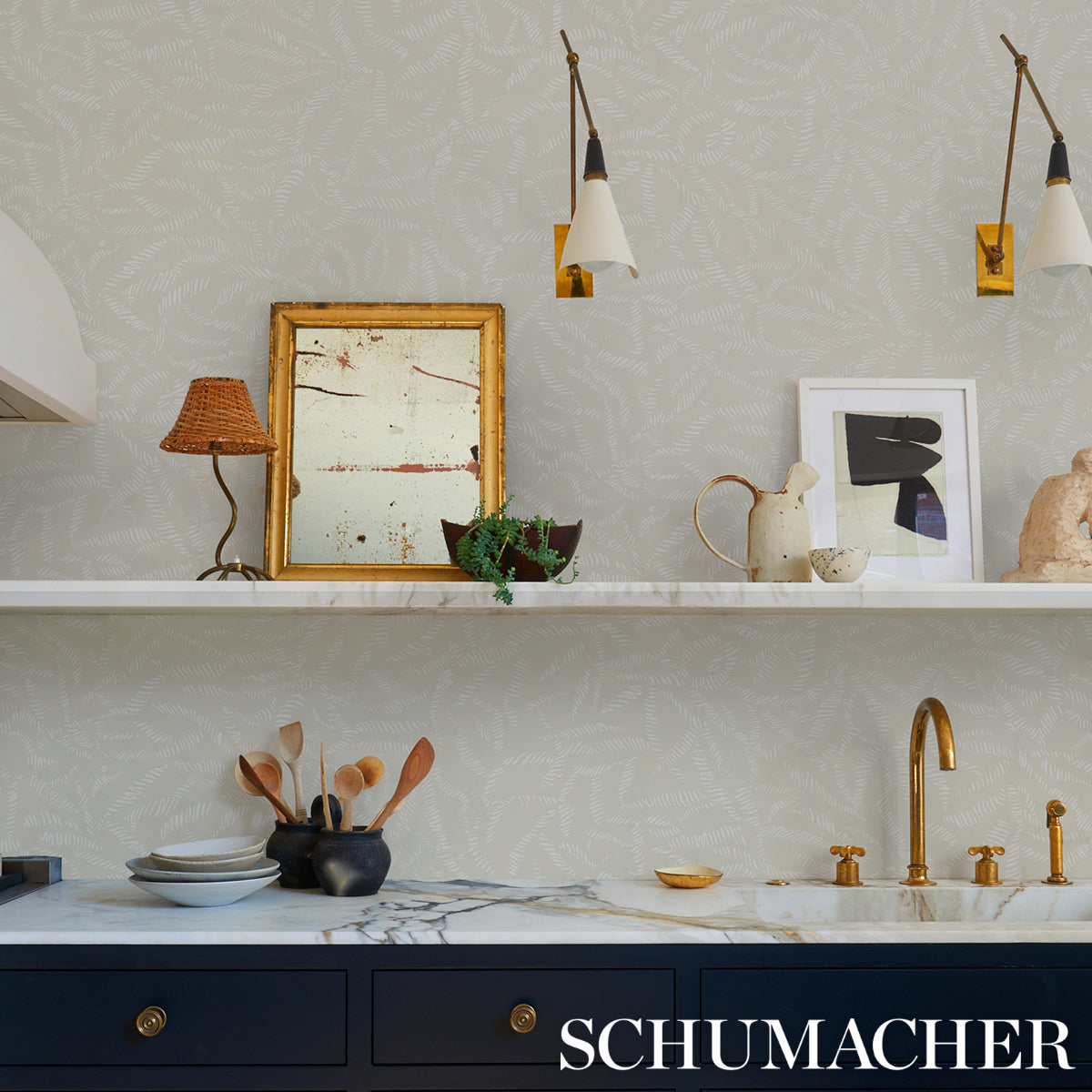 Modern kitchen with marble counter, navy cabinets, brass faucet, framed art, ceramic teapots and utensils under pendant lights.
