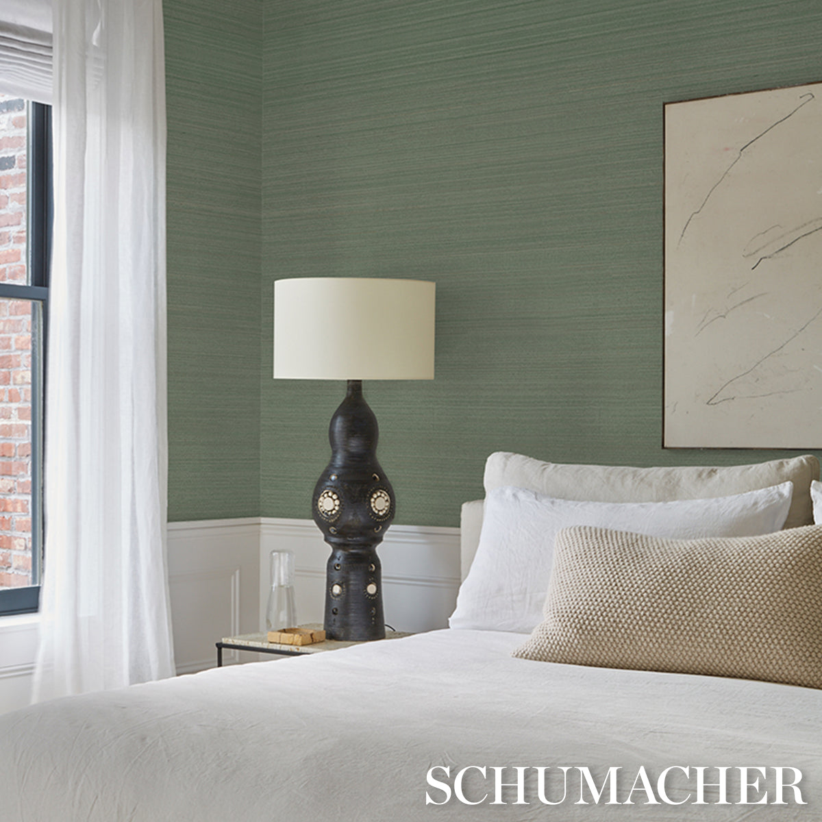Dark ceramic table lamp with circular cutouts on a nightstand beside white bedding and a green textured wall.