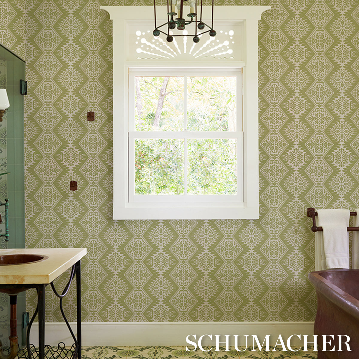 Green damask wallpaper in a vintage bathroom; white-framed window, brass fixtures, sink and tub.