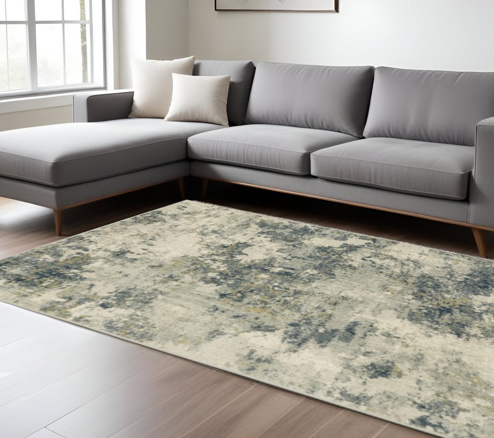 Gray L-shaped sectional sofa with light wood legs and an abstract blue-gray area rug in a bright living room.