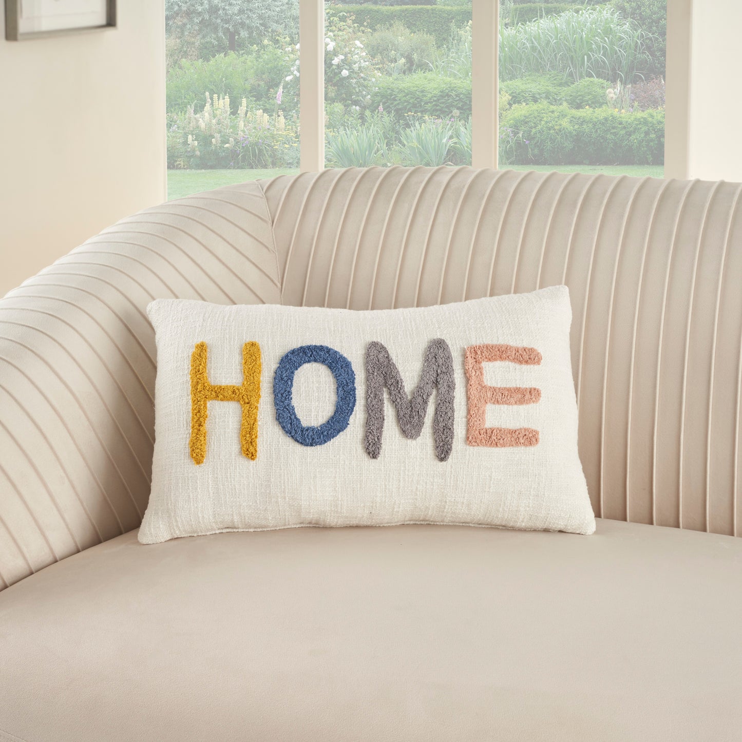 Beige striped sofa with a white textured pillow embroidered HOME in yellow, blue, gray and peach.