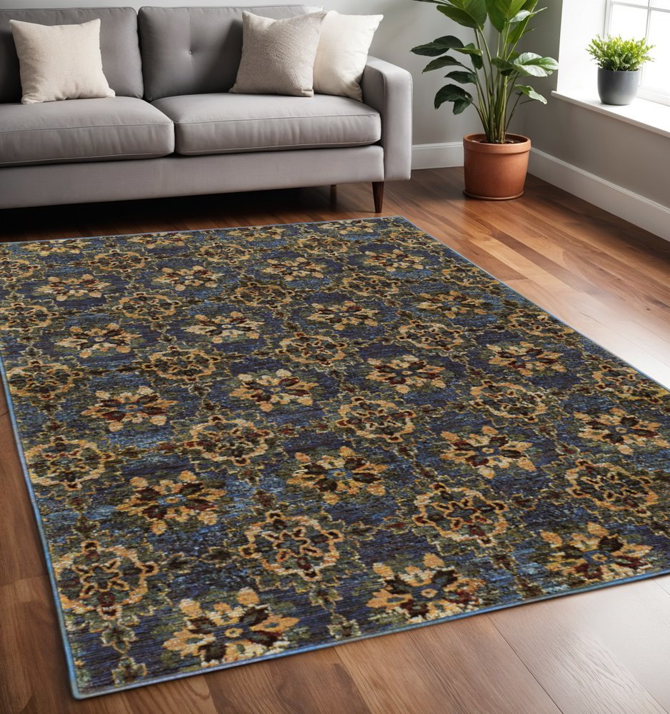 Ornate blue and gold oriental area rug on hardwood floor beside a gray sofa with cream cushions and a potted plant.