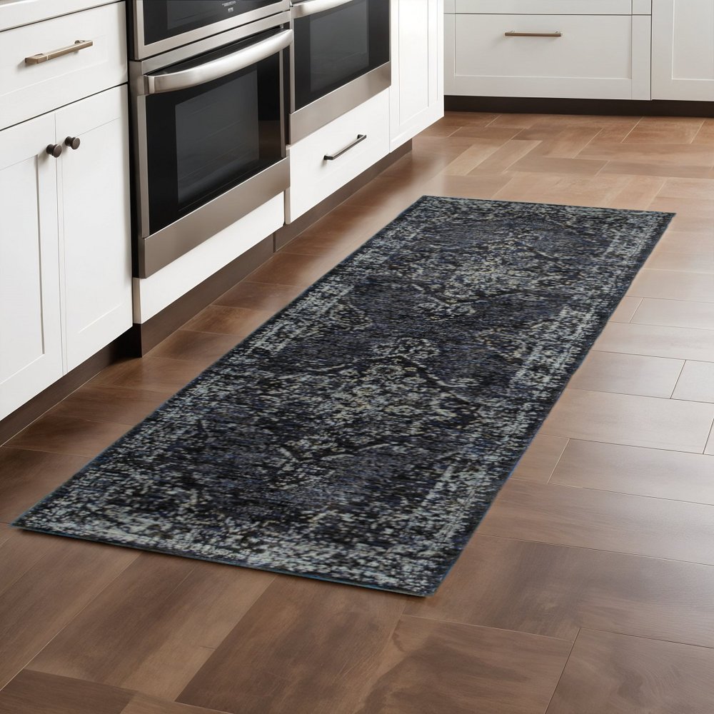 Dark blue distressed runner rug with pattern on brown hardwood kitchen floor beside white cabinets and stainless ovens.