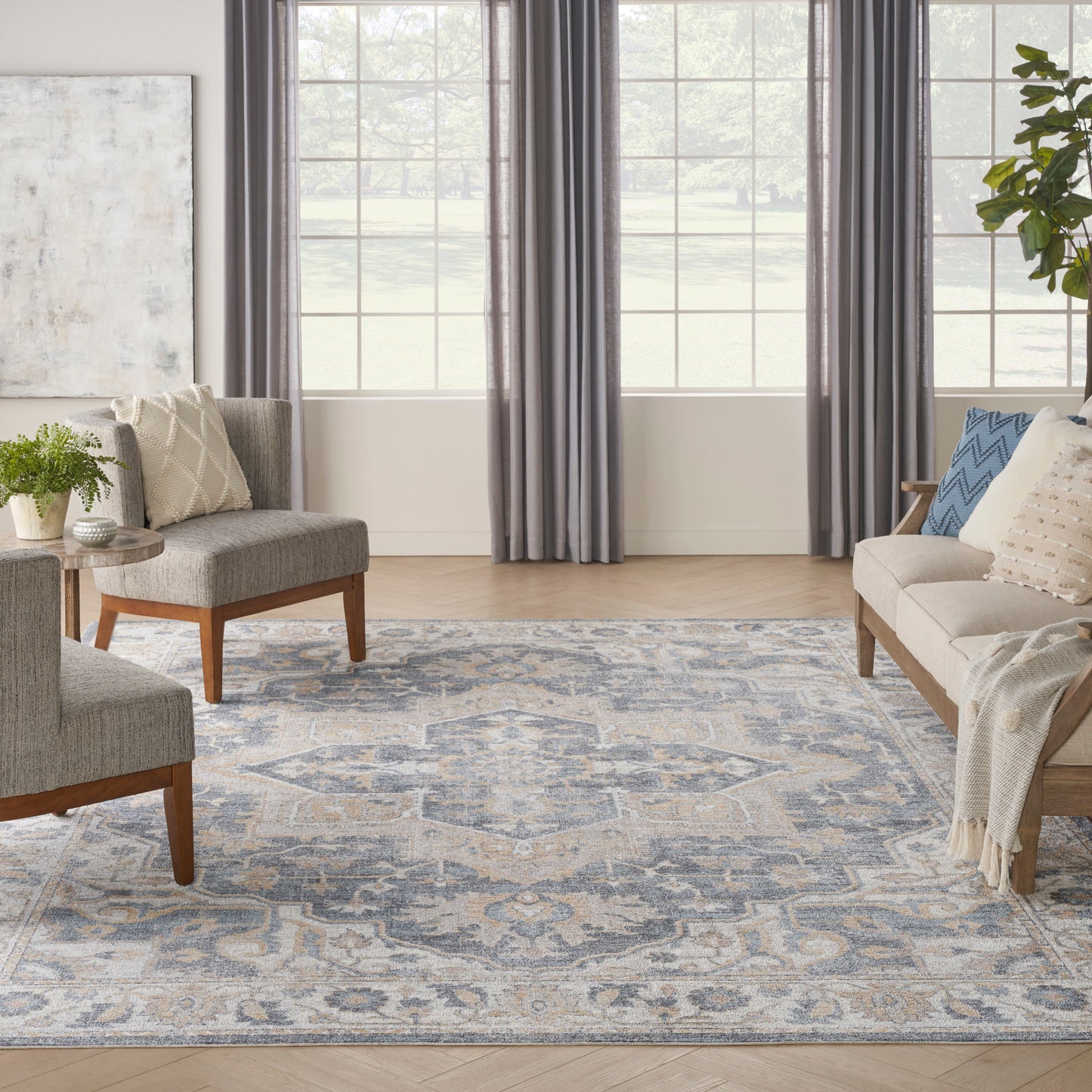 Cozy living room with blue-gray patterned rug, grey upholstered chairs, beige sofa, wooden legs, plant, and large windows.