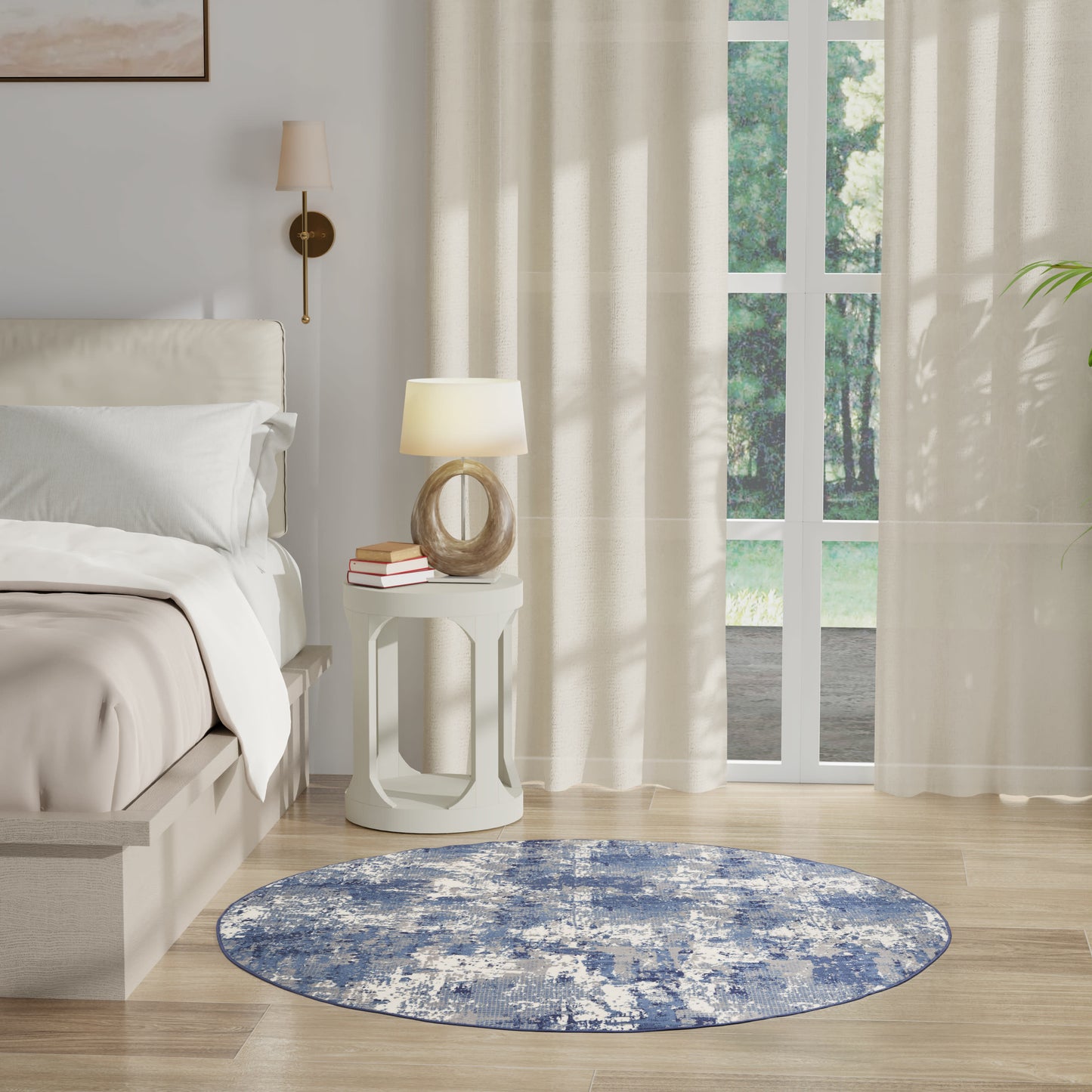 Cream and white bedroom with round blue distressed rug, nightstand, curved lamp, sheer curtains, and wooden floor.