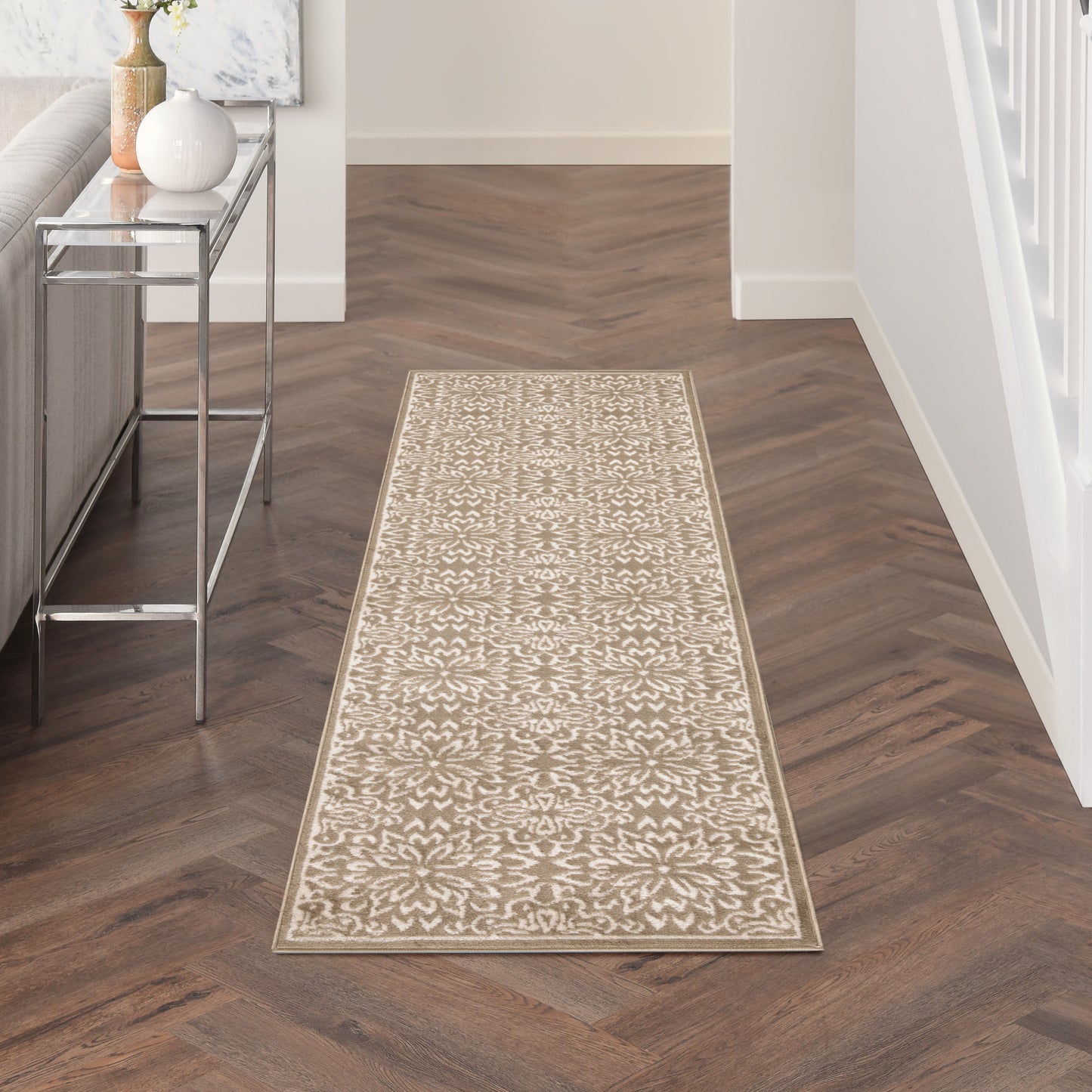 Cream floral-patterned hallway runner with a beige border on a dark herringbone floor beside a glass console table.