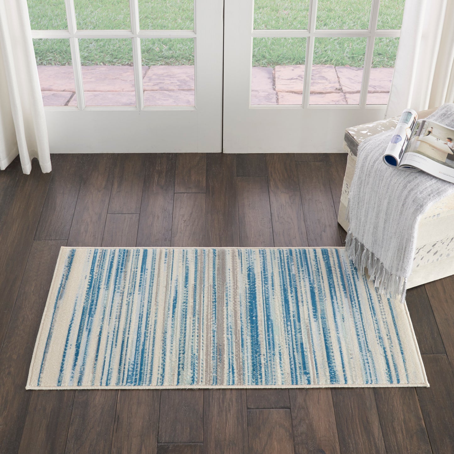 Rectangular woven rug with blue and cream vertical stripes on dark wood floor.