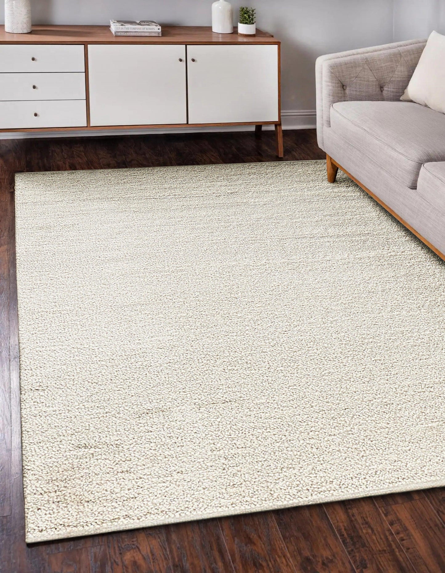 Rectangular cream textured area rug on dark wood floor with white-and-wood sideboard and beige sofa.