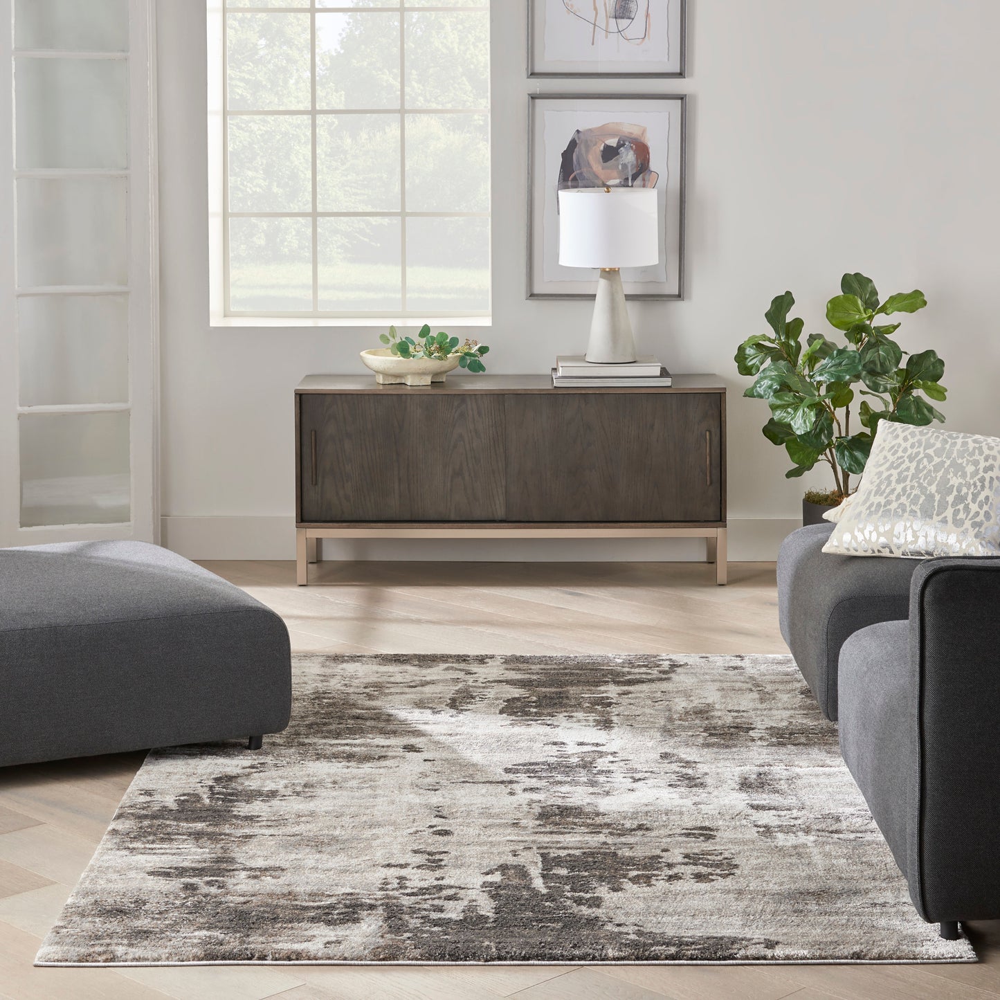 Modern living room: dark wood console with white lamp, framed art, green plant, gray sofas, & abstract gray rug, 5' x 7'.
