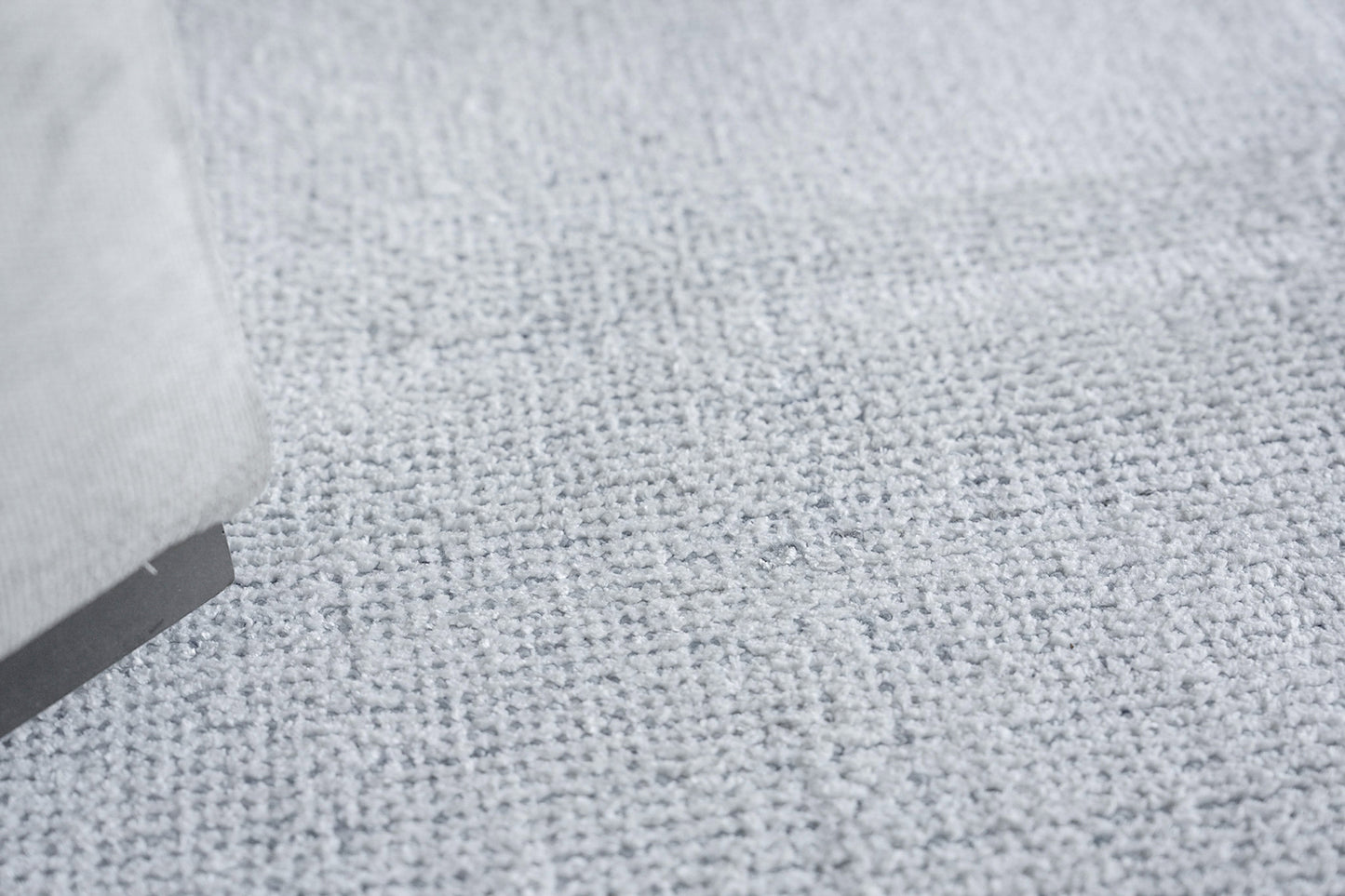 Close-up of light gray loop-pile rug with a gray fabric sofa leg at the edge