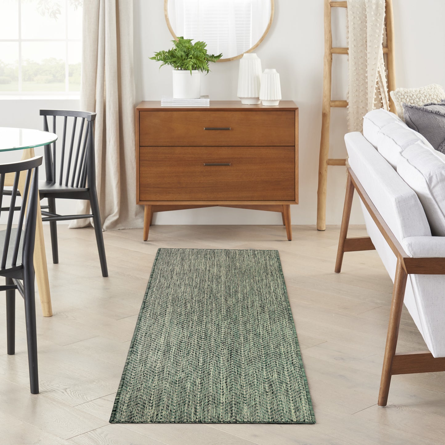 Green textured chevron rug runner in a light wood living room with a mid-century dresser and white sofa.