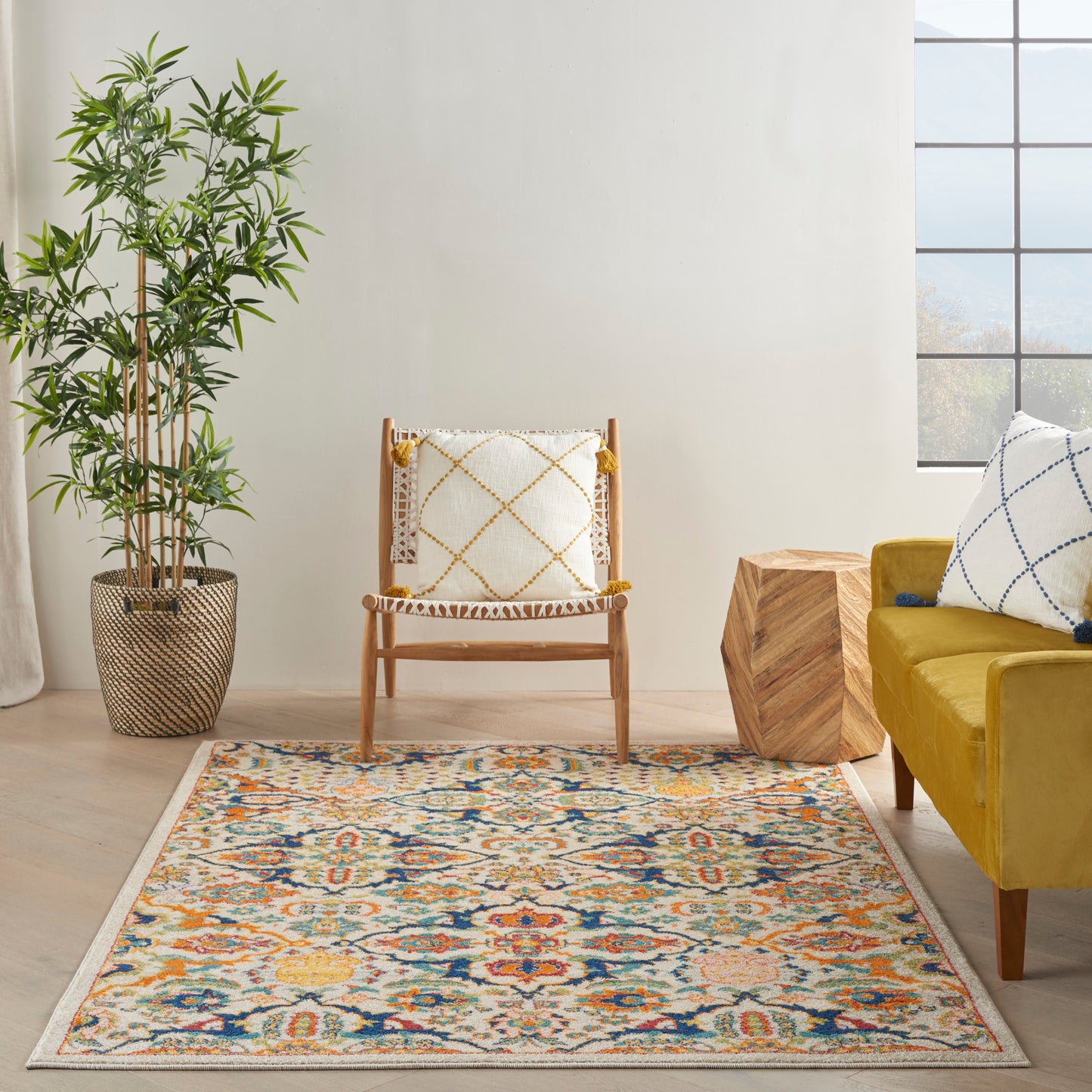 Colorful patterned rug in a bright living room with a mustard sofa, wooden chair, tassel-trimmed pillow, and greenery.