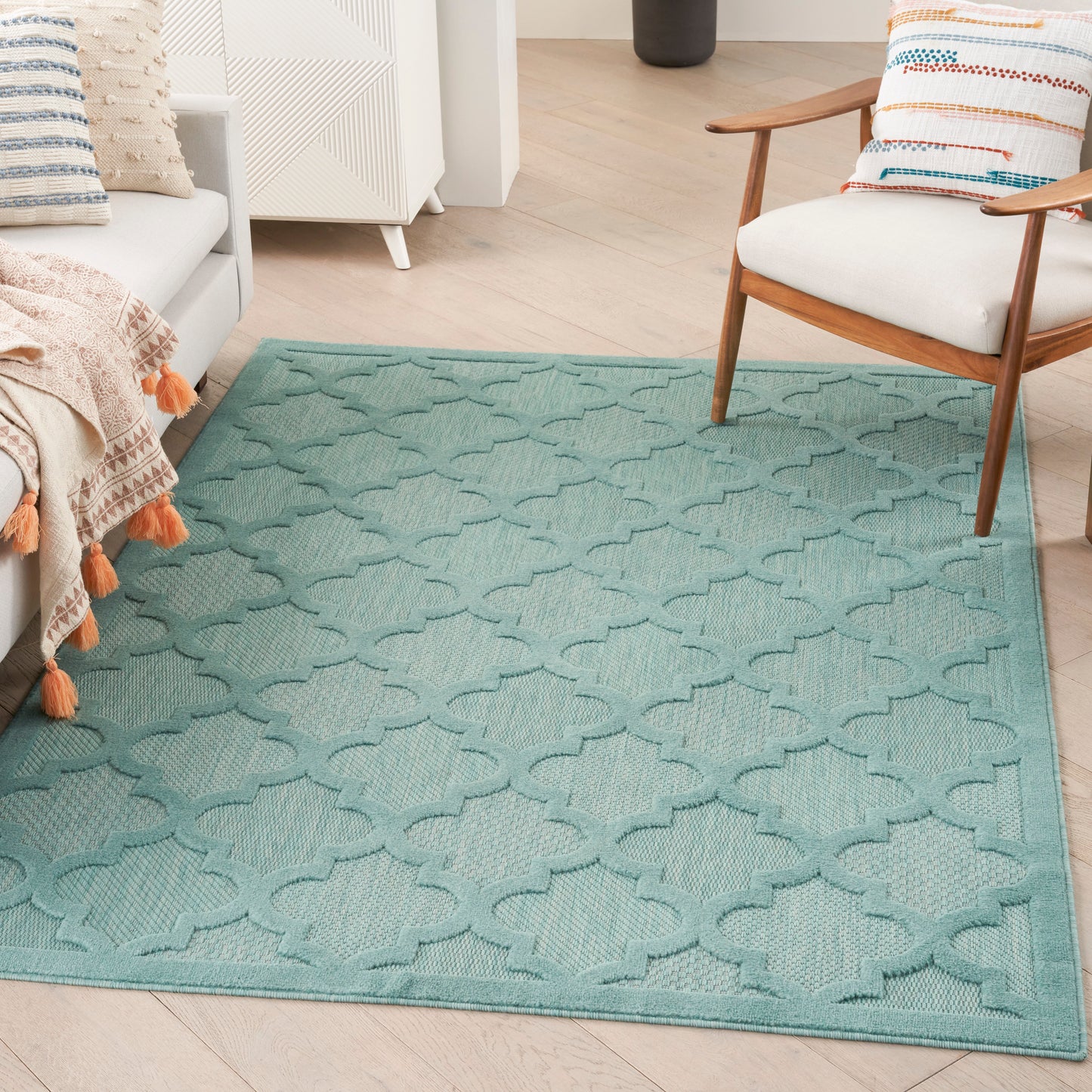 Teal geometric trellis rug on light wood floor in a living room with a white sofa and wooden armchair.