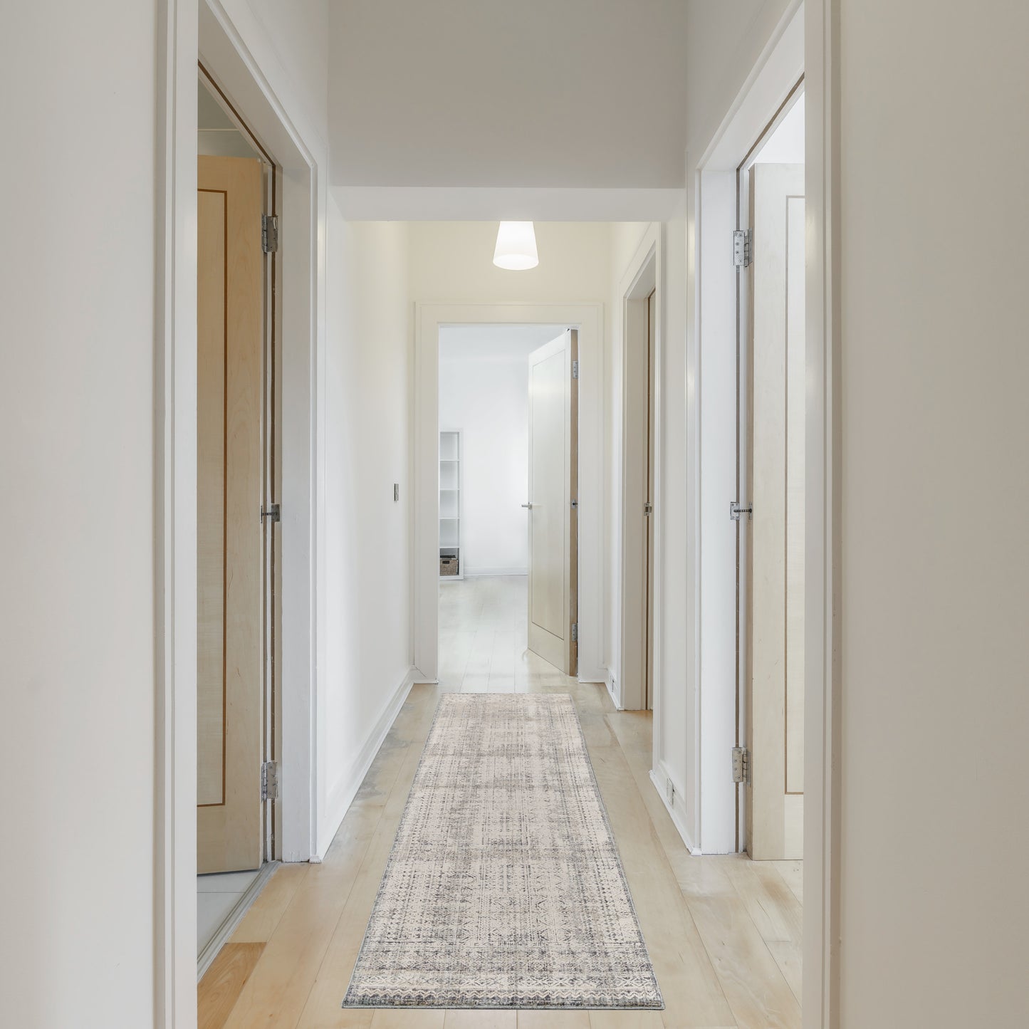 Bright minimalist hallway with white walls, light wood doors on both sides, and a gray patterned runner.