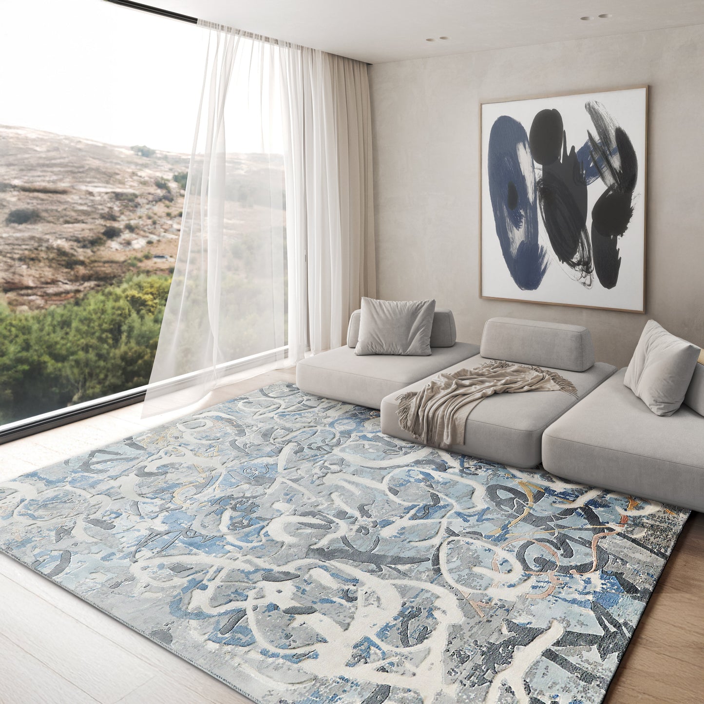 Contemporary living room featuring a light gray sectional, abstract blue handloomed rectangle rug (6' x 9'), sheer curtains, and blue-black wall art.