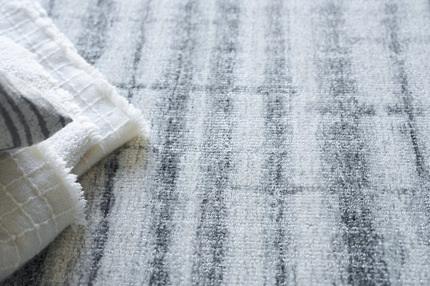 Light gray and white striped rug with soft pile; folded white waffle-weave towel on the left.