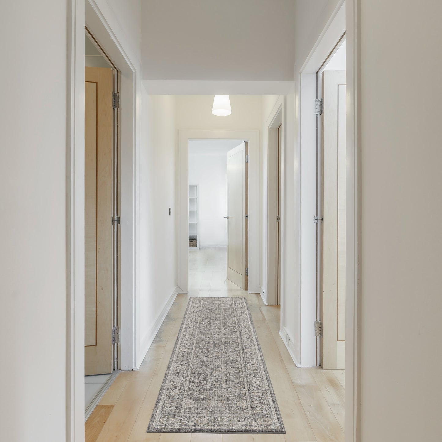 Bright white hallway with light wood doors, beige walls, and a long gray patterned runner rug under soft overhead light.