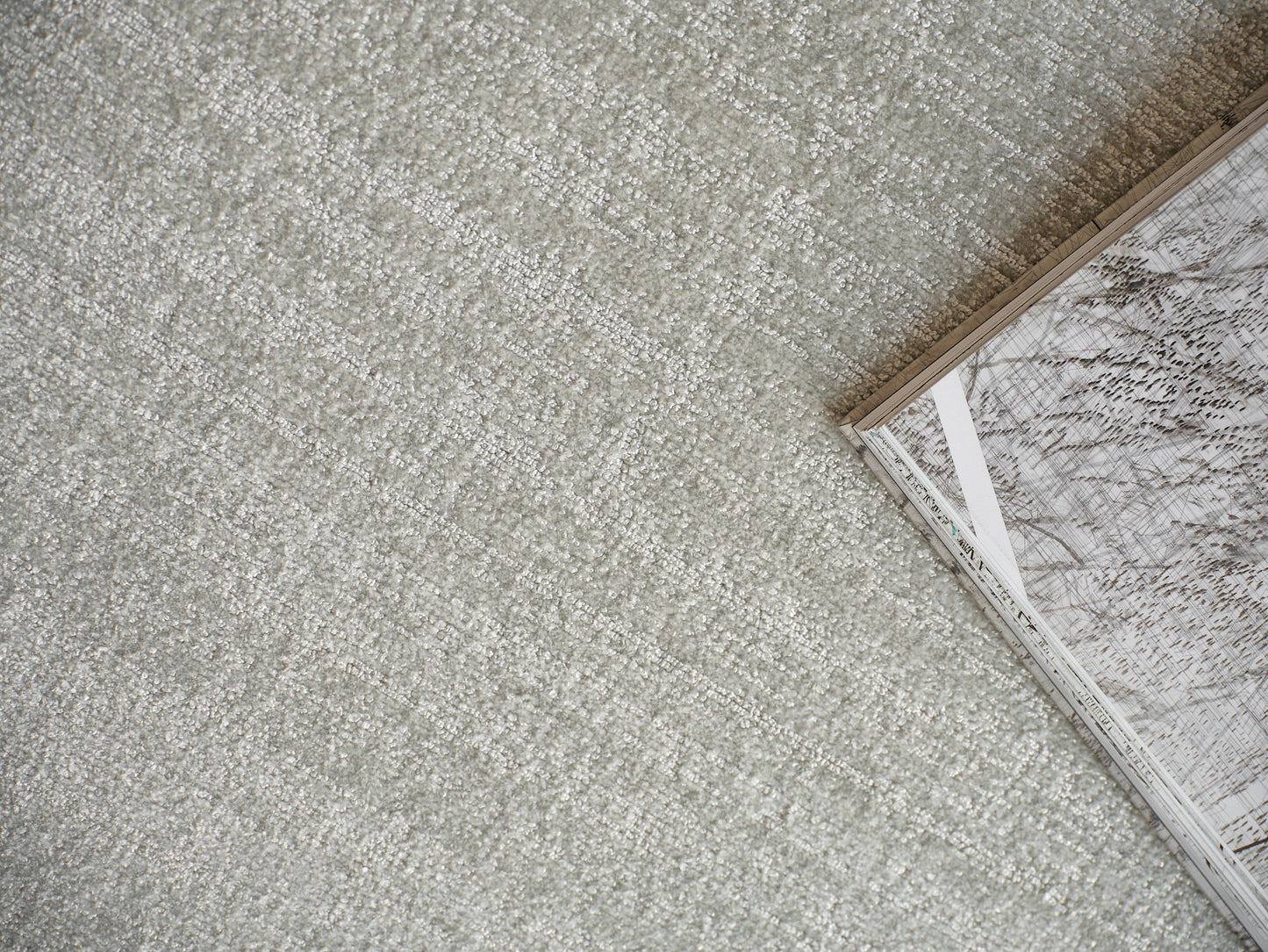 Soft gray textured carpet with a corner-open magazine featuring marble-patterned pages.