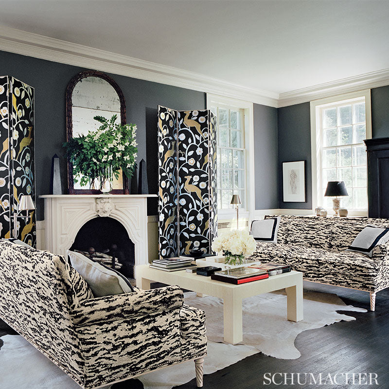 Elegant living room with navy walls, white mantel, black floral screens, zebra-print sofas, white coffee table, cowhide rug.
