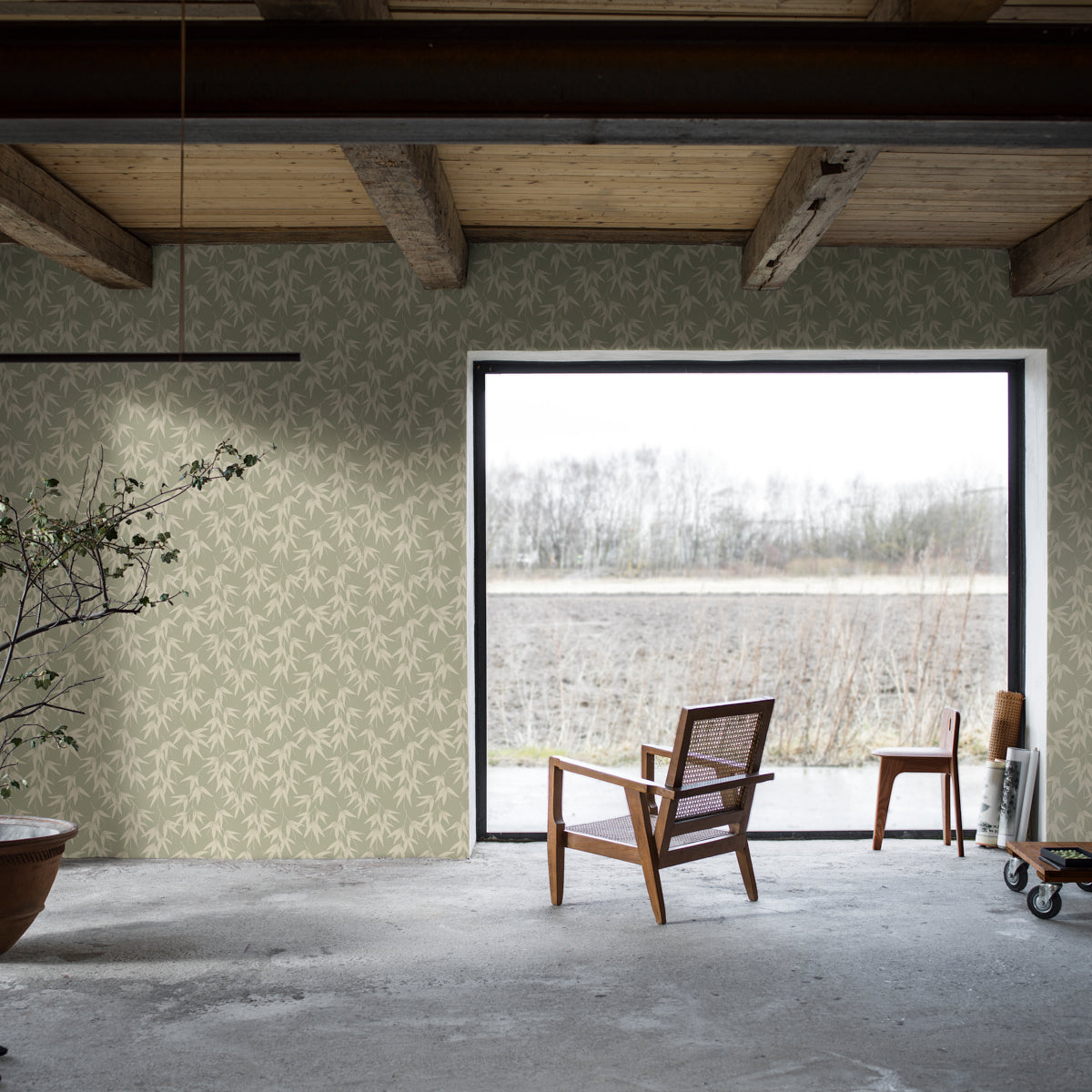Industrial living space with pale green leaf-pattern wallpaper, exposed beams, and two wooden chairs by a doorway to a field.