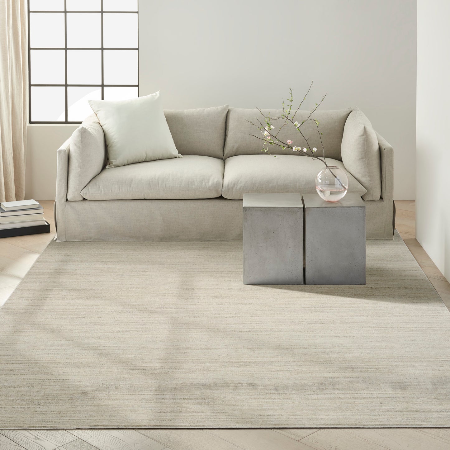 Beige rug in a minimalist living room with concrete cube side tables and a vase with branches.